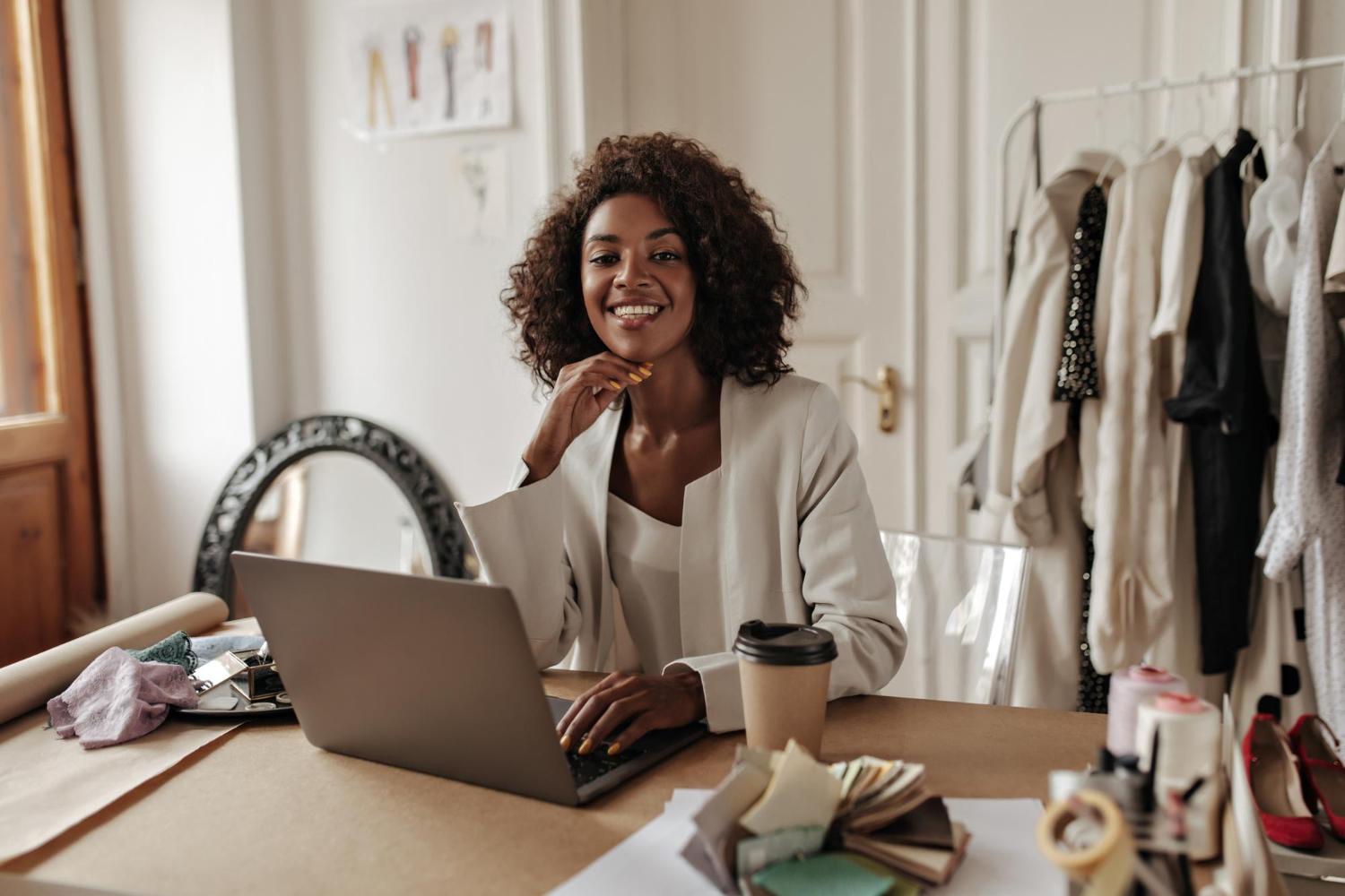 charming young darkskinned woman stylish jacket blouse smiles looks camera works laptop poses office
